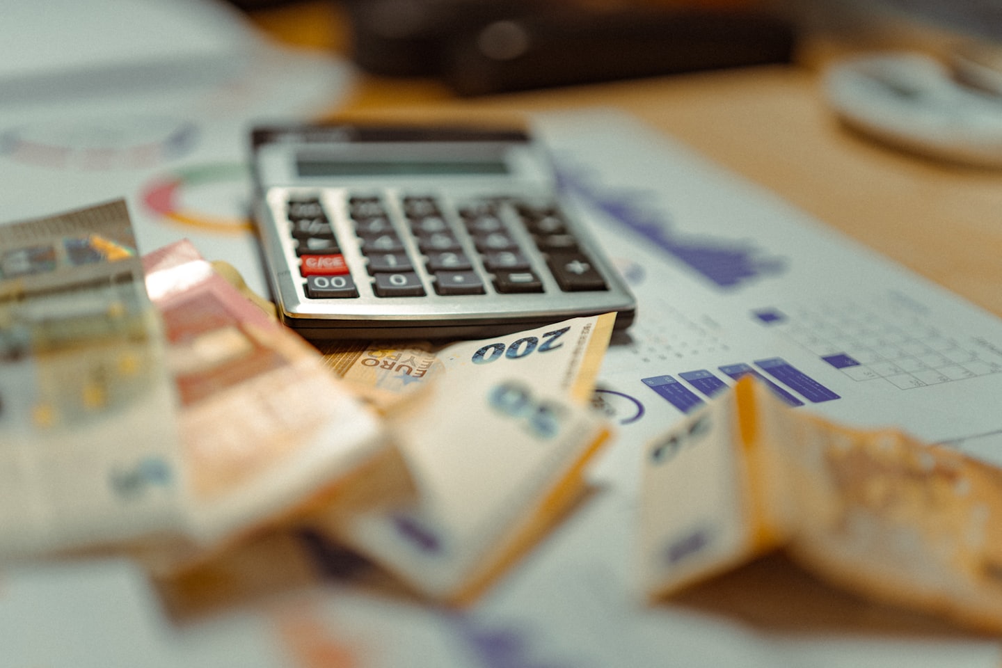 Kalkulator, banknoty euro i wykresy finansowe na biurku.